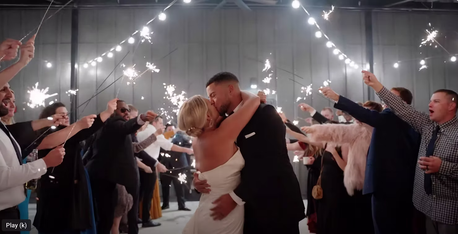 Bride and groom kiss during a sparkler exit under string lights