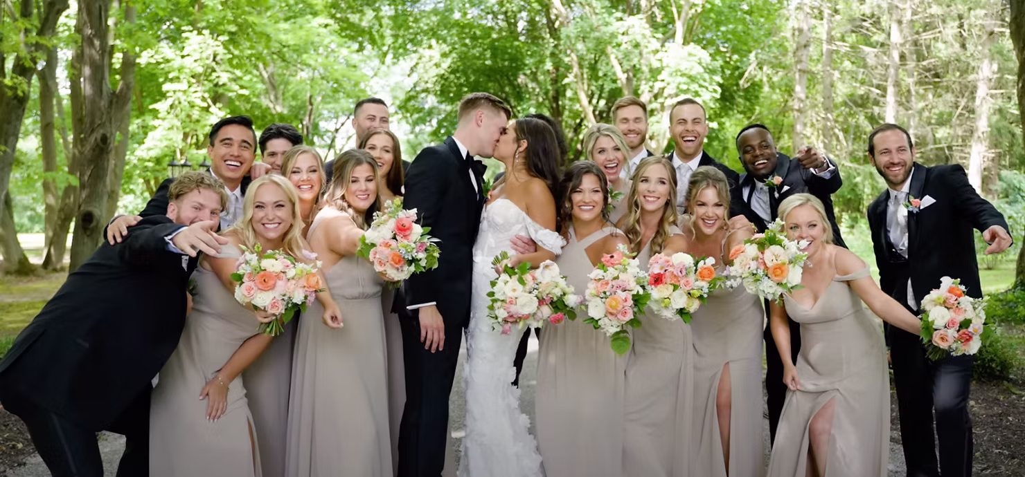 Large wedding party posing together in a tree-lined garden