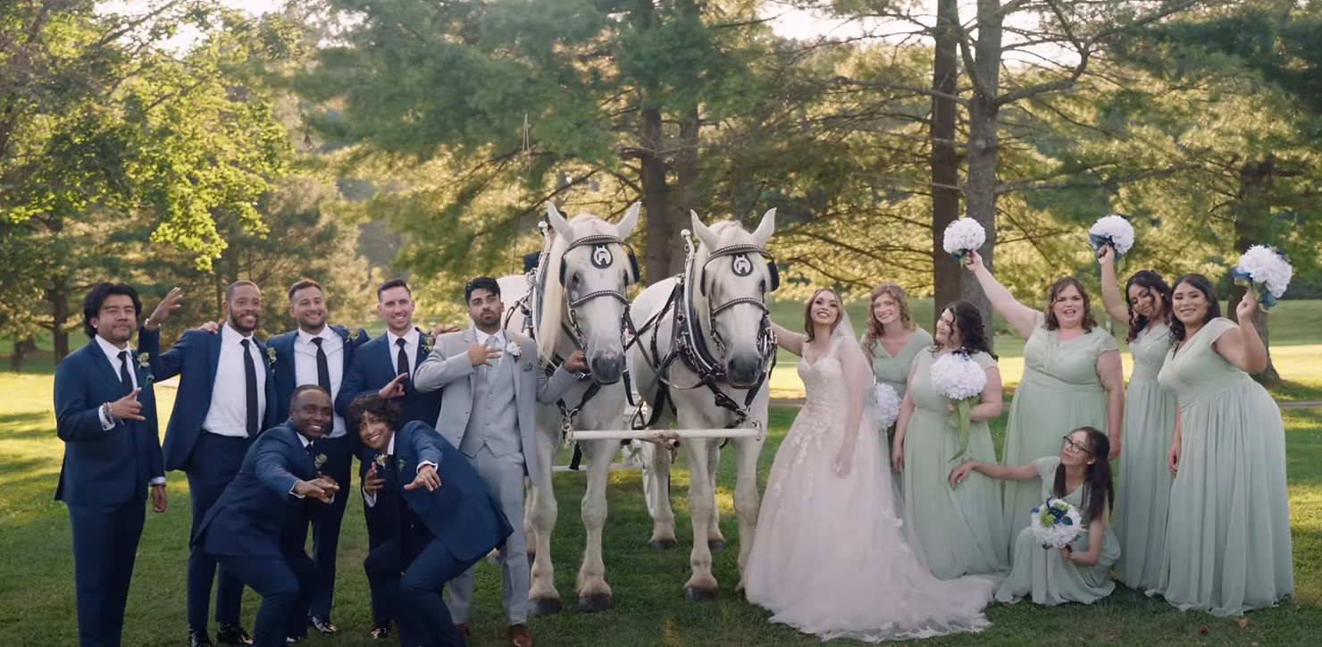 Wedding party posing with white horses in a green garden